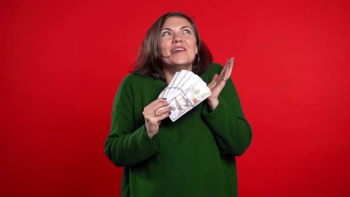 满意的快乐兴奋的女人显示钱-红墙上的美元钞票。成功、收获、胜利的象征。慢动作