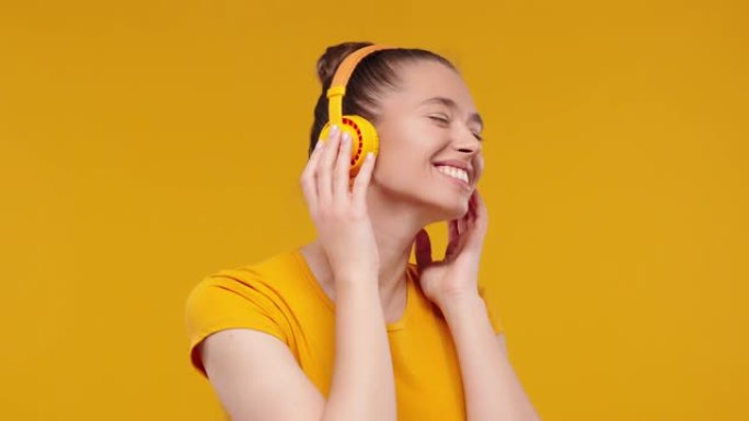 漂亮女孩通过耳机听音乐和跳舞的肖像孤立在工作室黄色背景