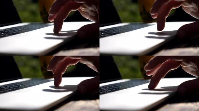 男性手指在笔记本电脑的触摸板上触摸和滑动。在户外笔记本工作的面目全非的人。和某人聊天或浏览互联网的人