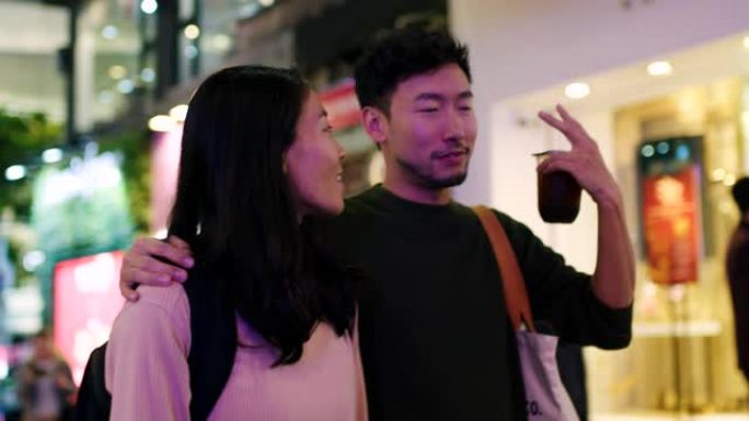 SLO MO手持中景，一对年轻夫妇在晚上穿越香港