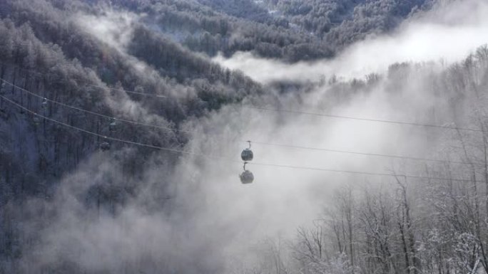 滑雪电梯在低地白色雪山云雾森林上空移动。无人机景观滑雪缆车将滑雪者和滑雪板运送到冬季自然景观上的避暑