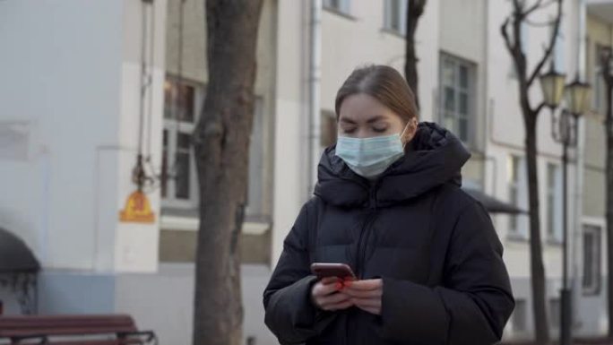 在空荡荡的欧洲街道上使用智能手机戴着防护医用口罩的女人的肖像。健康与安全、N1H1冠状病毒、新型冠状
