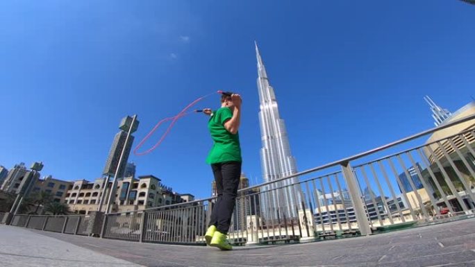 在迪拜的城市景观背景下，男子用跳绳跳跃。慢动作
