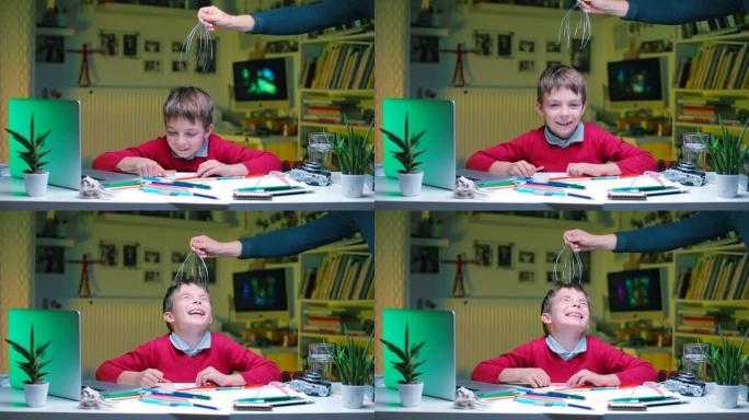 一个男孩坐在学校的桌子旁。一只手给他做头部按摩。