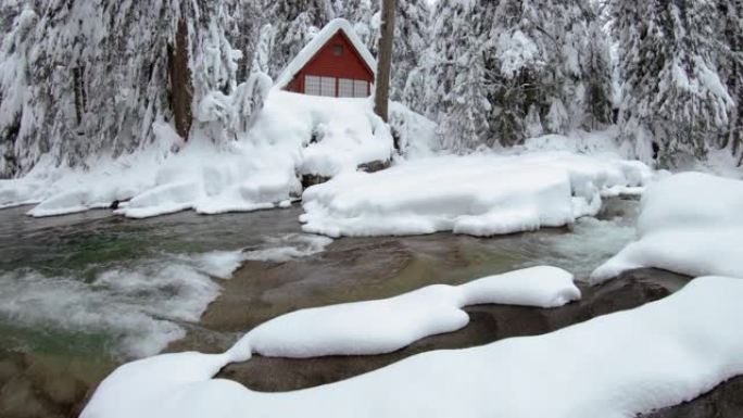 树林中的红色小屋被河水覆盖着冬天的雪