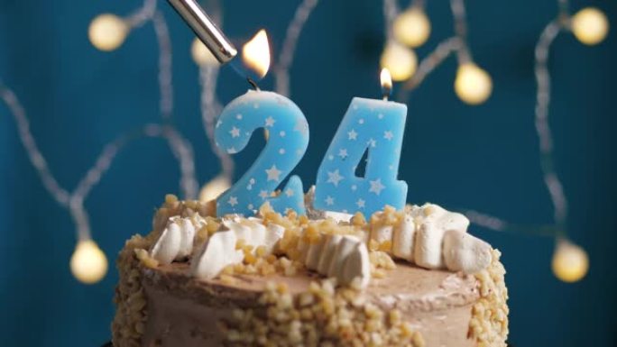 蓝色背景上有24号蜡烛的生日蛋糕。蜡烛着火了。慢动作和特写视图