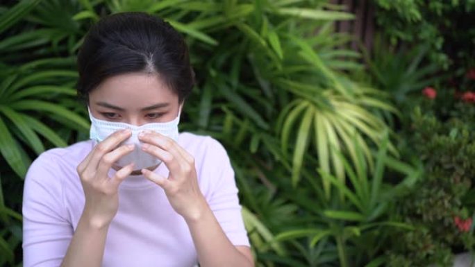 4k亚洲年轻女子戴口罩保护自己形成病毒大流行，细菌疾病和空气污染，绿叶灌木丛背景，covid19日冕