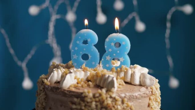 蓝色背景上有68号蜡烛的生日蛋糕。蜡烛着火了。慢动作和特写视图