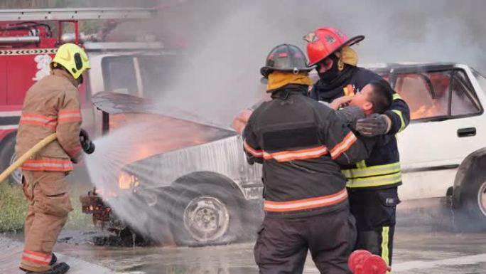 亚洲消防员穿着防火服，怀里抱着一个得救的男孩，消防员在消防演习中与汽车起火，并帮助火灾受害者概念。慢