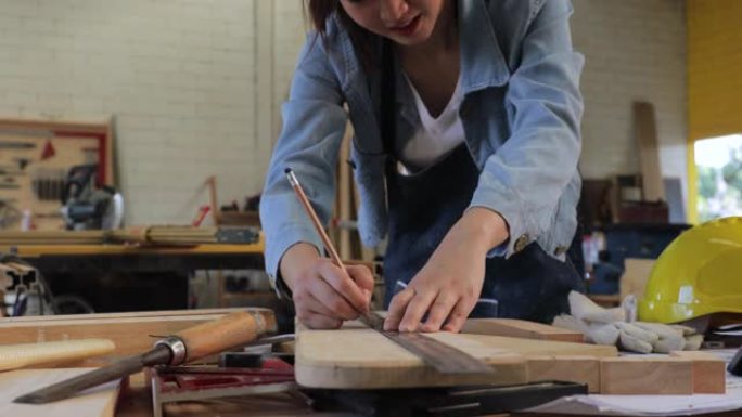 美丽的年轻木匠正在用尺子和铅笔在木板上画线，以便下次切割。木制工艺概念。