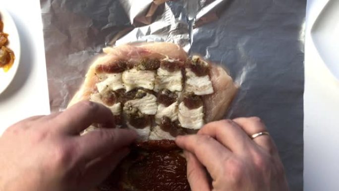一名男子将猪油，奶酪，萨拉米香肠和晒干的西红柿放在鸡肉上。滚。