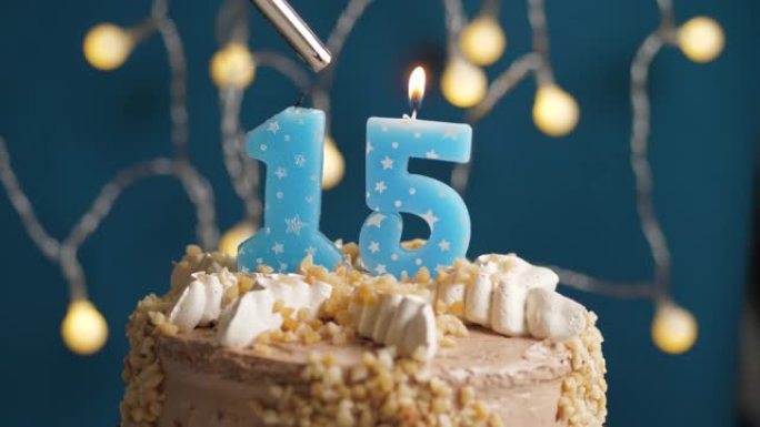 蓝色背景上有15个数字蜡烛的生日蛋糕。蜡烛着火了。慢动作和特写视图