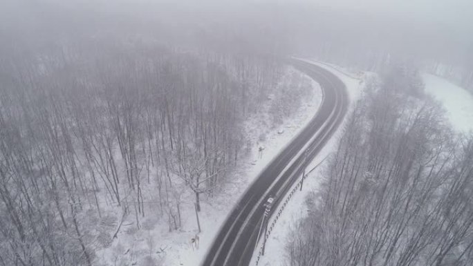 在降雪下驾驶高速公路穿过森林的汽车。无人机航拍视频与电影复杂的摄像机运动，上升和前进，跟随汽车。