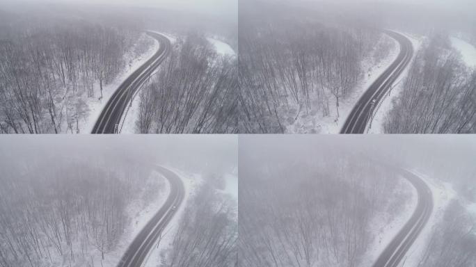 在降雪下驾驶高速公路穿过森林的汽车。无人机航拍视频与电影复杂的摄像机运动，上升和前进，跟随汽车。