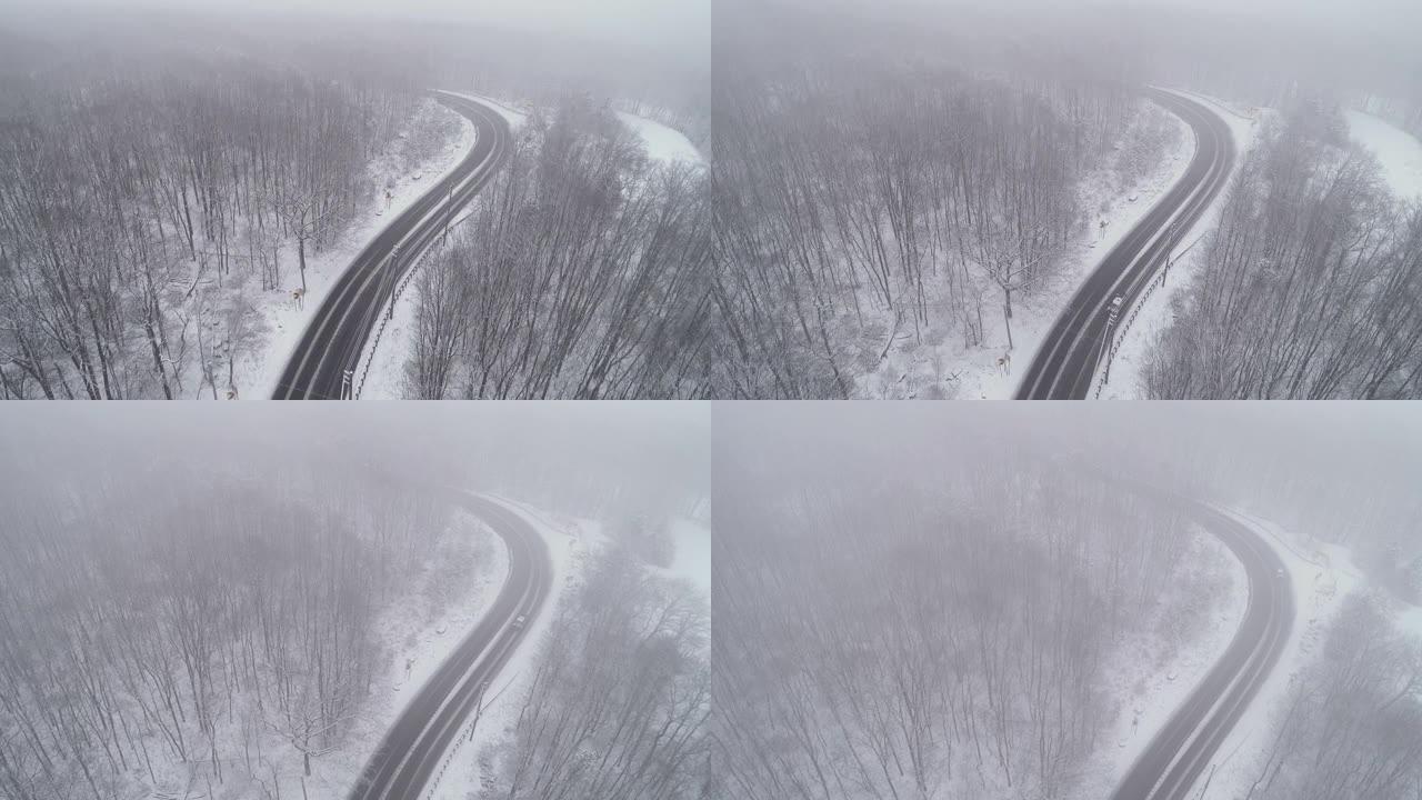 在降雪下驾驶高速公路穿过森林的汽车。无人机航拍视频与电影复杂的摄像机运动，上升和前进，跟随汽车。