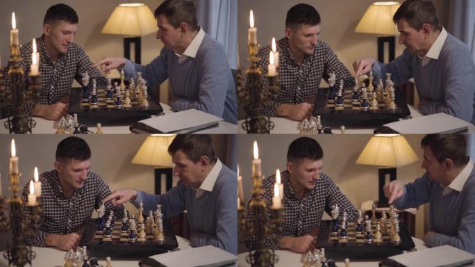 聪明的中年白人男子教成年儿子下棋的肖像。两个人在家过夜。生活方式、爱好、智力