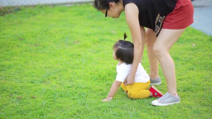 亚洲母亲从草地上抱起婴儿