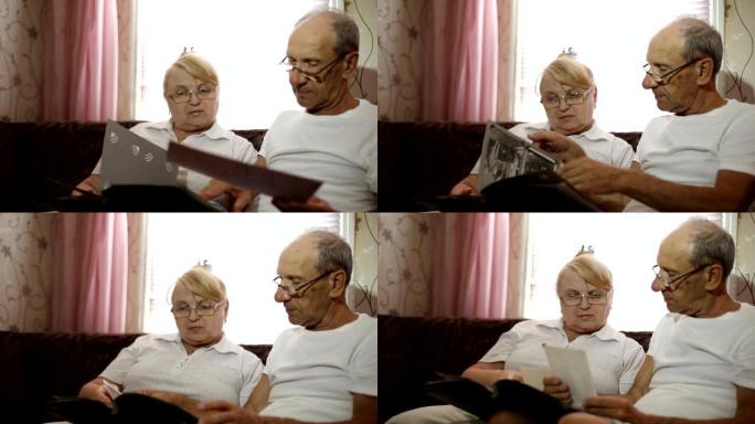 成年夫妇坐在沙发上看着他们的照片。夫妻戴着眼镜看他的专辑。
