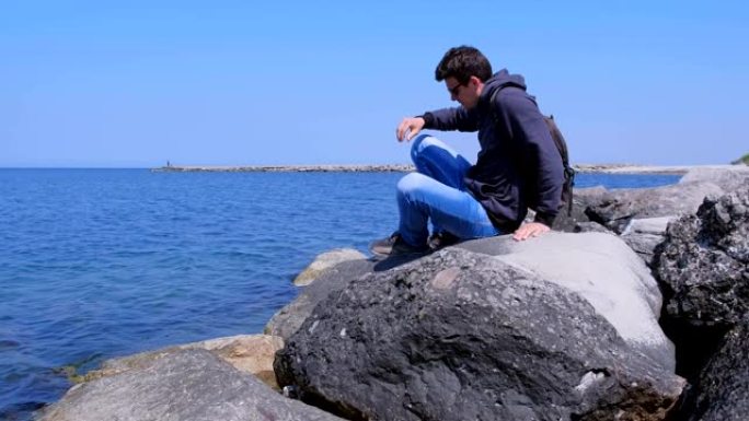 男人旅行者来到海边度假时坐在巨大的石头上欣赏海景。