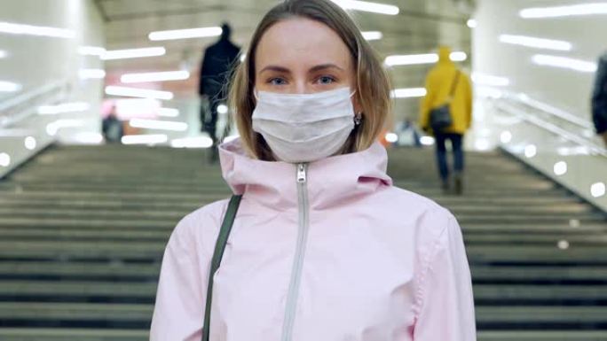 戴着保护性无菌医用口罩的女人看着地铁站的摄像头，病毒，大流行冠状病毒概念