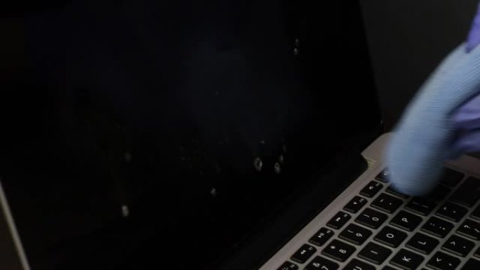 一个戴着橡胶手套的男人正在清洁他的笔记本电脑。一块特殊的布擦拭笔记本电脑屏幕。保护工作设备免受病毒感