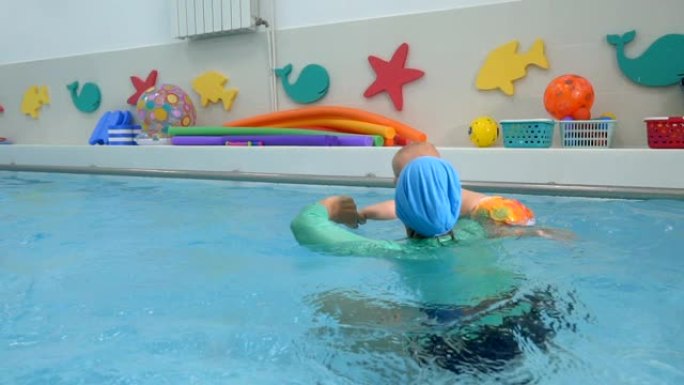 一名女教练在儿童游泳池的水中与婴儿进行体育锻炼。她把孩子抱在怀里。他们玩耍和大笑。婴儿游泳。特写