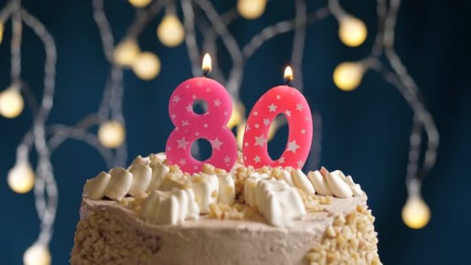 蓝色背景上有80号粉色蜡烛的生日蛋糕。蜡烛吹灭了。慢动作和特写视图