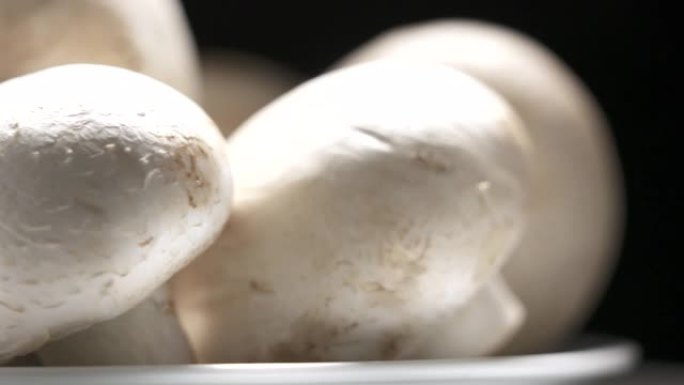 新鲜的生白色香菇在黑色背景上旋转特写。