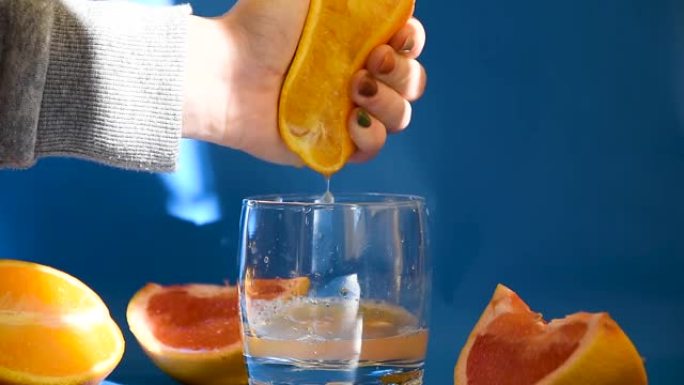用手挤出新鲜的橙子。柑橘汁从果肉中排出，并在蓝色背景上滴落