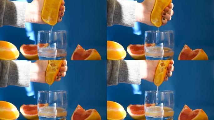 用手挤出新鲜的橙子。柑橘汁从果肉中排出，并在蓝色背景上滴落