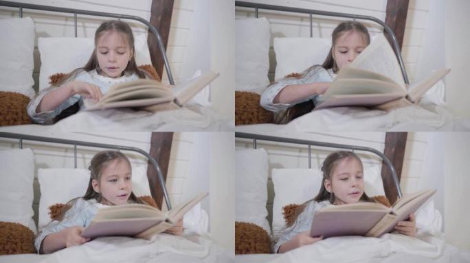 漂亮的高加索女孩躺在床上看书的肖像。聪明的孩子晚上睡觉。就寝时间，爱好，休闲。