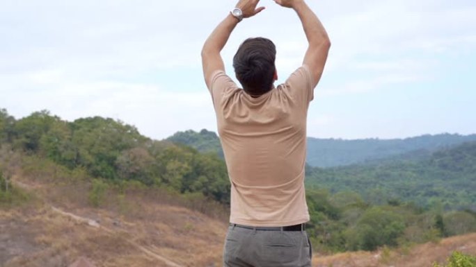 高清慢动作兴奋的年轻人徒步旅行者站在日落时的山峰上，双臂伸向空中，脸上露出快乐的脸。赢得人生成就和成