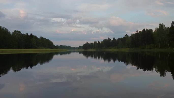 平静的夏夜日落美景。湖岸绿树和植物反射在水晶干净的镜面水面。天空覆盖着厚重的雷云。