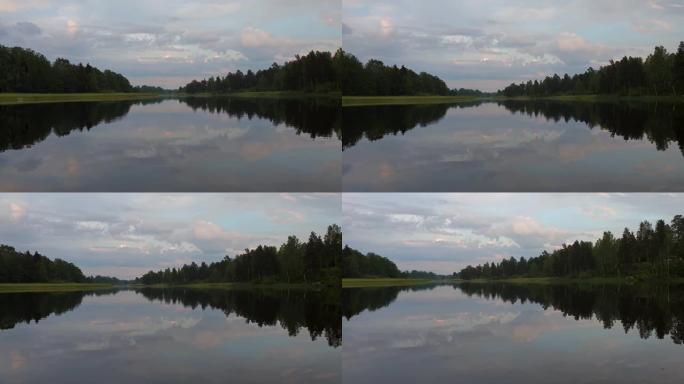 平静的夏夜日落美景。湖岸绿树和植物反射在水晶干净的镜面水面。天空覆盖着厚重的雷云。