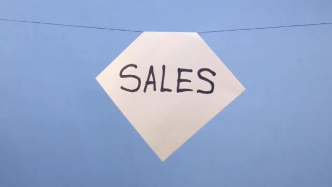 一名男子在蓝色背景上悬挂一张白纸，上面刻有黑色铭文 “sales”
