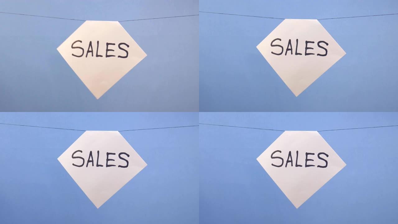 一名男子在蓝色背景上悬挂一张白纸，上面刻有黑色铭文 “sales”