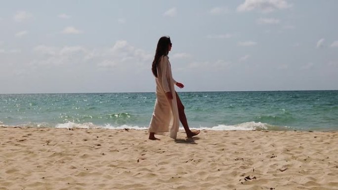 年轻漂亮的性感女士，穿着红色泳衣和白色长裙，戴着太阳眼镜，走在海边的沙滩海岸线上。度假放松，暑假，浪