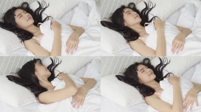 美丽的亚洲年轻女子躺在床上睡觉，头在枕头上舒适快乐地在卧室移动相机，女孩以放松和休闲为健康，生活方式
