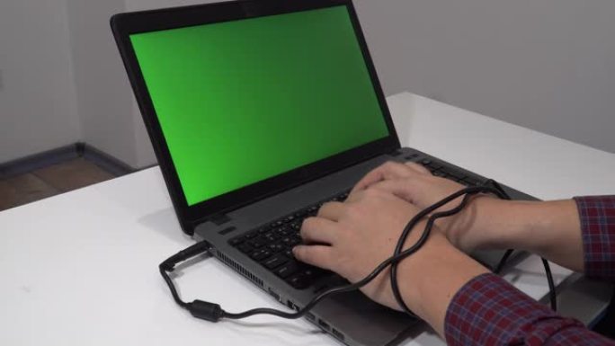 现代问题概念。男子在笔记本电脑上打字，双手纠结在电缆中