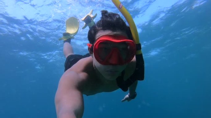 穿着红色潜水镜的亚洲年轻人在水面上，自由潜水，在海洋中央，浮潜晴天，水下镜头，清澈的水，旅行冒险探索