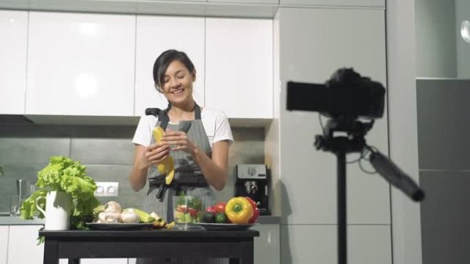 迷人的年轻女子在家里的厨房里用数码相机录制了一段关于健康饮食的视频。视频博客和社交媒体概念
