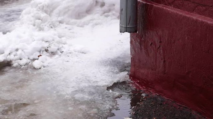 从建筑物排水沟管道滴落的融化雪的特写镜头。