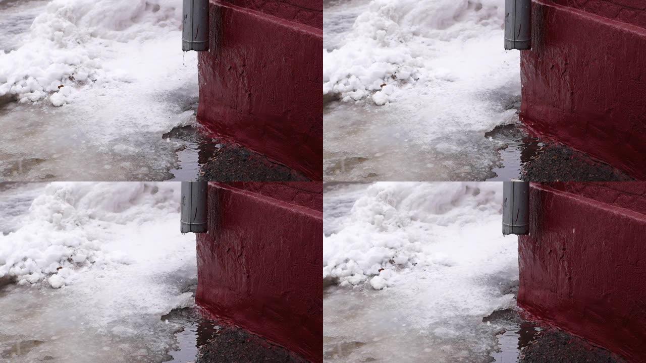 从建筑物排水沟管道滴落的融化雪的特写镜头。