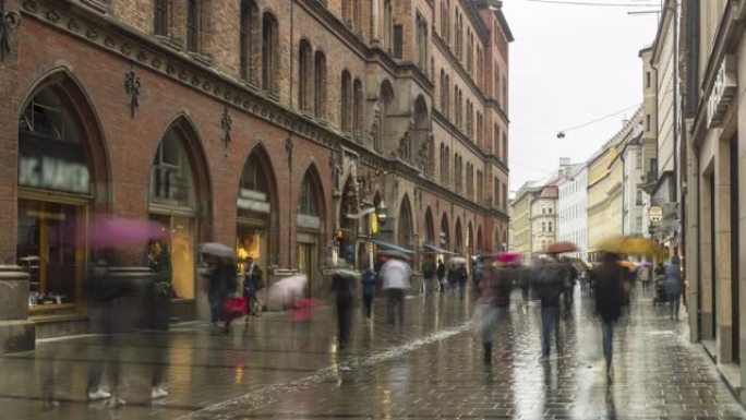 德国慕尼黑下着雨，人们走在购物街上，但游客仍然撑着伞观光