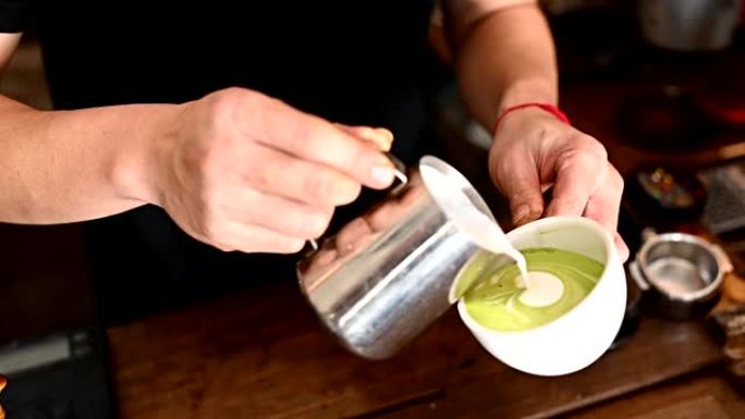 咖啡师手的短打镜头，试图将蒸牛奶倒入热绿茶中，以制作拿铁艺术。