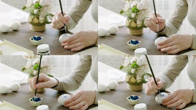 画复活节彩蛋的女人特写。女性的手在鸡蛋上画了蓝色的花卉图案，彩绘成白色。4K