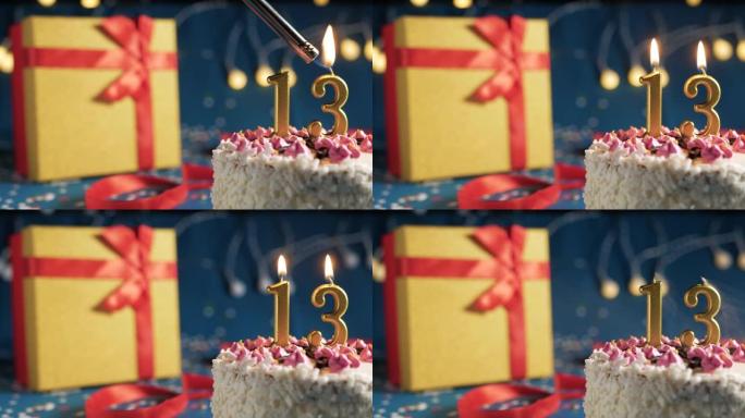 白色生日蛋糕13号点火器燃烧的金色蜡烛，蓝色背景带灯和用红丝带绑起来的礼物黄色盒子。特写
