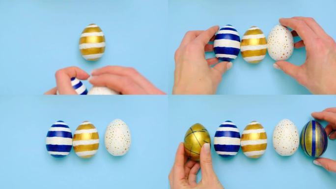 女性的手在蓝色桌子上放了5个复活节彩蛋。鸡蛋时尚彩色经典蓝色、白色和金色。复活节快乐。最小风格。顶视