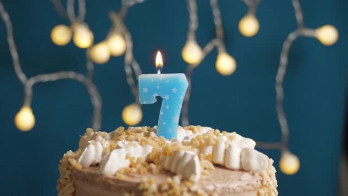 蓝色背景上有7号蜡烛的生日蛋糕。蜡烛吹灭了。慢动作和特写视图