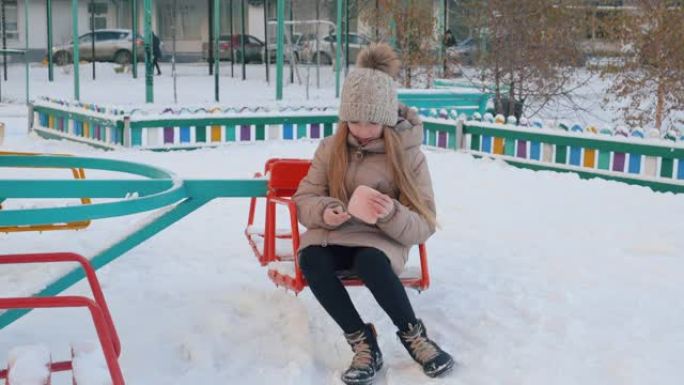 十几岁的女孩在冬季散步时在下雪的孩子们的地面上发现了钱包。年轻女孩拿钱包躺在冬天在城市的雪地上。